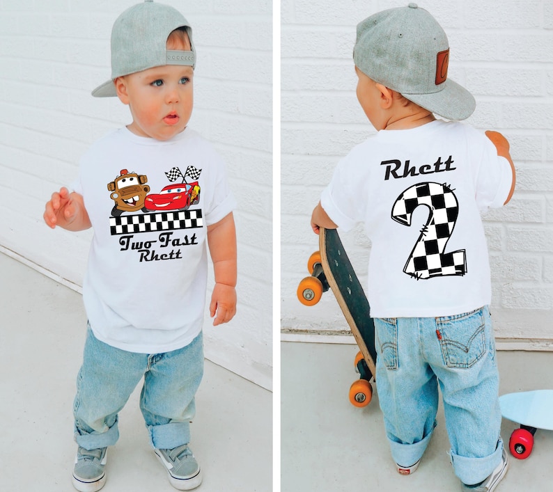 May include: White toddler t-shirt with a graphic of Mater and Lightning McQueen from the movie Cars, with the text "Two Fast Rhett". The back of the shirt has a checkered number 2 and the name "Rhett". The child is wearing blue jeans and a gray baseball cap.