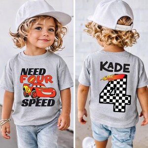 Op de afbeelding: Een grijs gem&ecirc;leerd T-shirt met korte mouwen, voorzien van een rode raceauto-afbeelding met de tekst "NEED FOUR SPEED" op de voorzijde en de naam "KADE" boven een groot geblokt cijfer "4" met een "95" bliksemschicht op de achterzijde.
