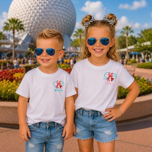 May include: Two white t-shirts featuring a small graphic of a red polka-dot bow and a teal infinity symbol on the chest. The left shirt has the text Bro in blue, and the right shirt has the text Sis in pink. Both shirts have short sleeves and a crew neck.