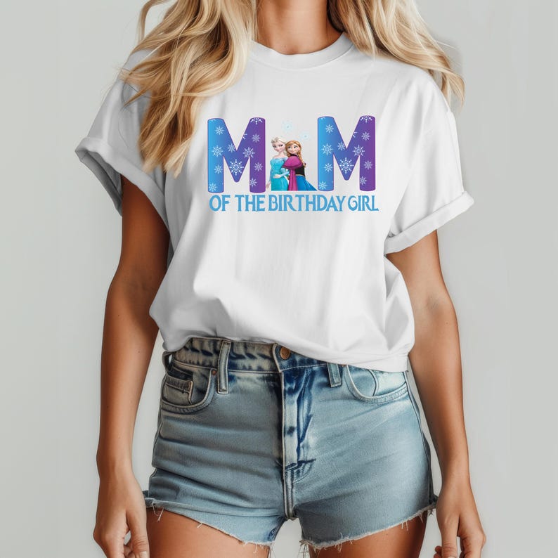 K&ouml;nnte beinhalten: Wei&szlig;es T-Shirt mit dem Text "MOM OF THE BIRTHDAY GIRL" in Blau und Lila. Das Design enth&auml;lt eine Grafik von zwei Zeichentrickfiguren. Das T-Shirt wird von einer Person getragen, die Jeansshorts tr&auml;gt.