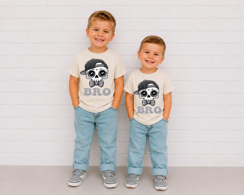 May include: Two cream-colored short-sleeve t-shirts featuring a graphic of a skull wearing a black baseball cap and a bow tie, with the word BRO printed in grey underneath. The shirts are paired with light blue denim jeans and grey sneakers.