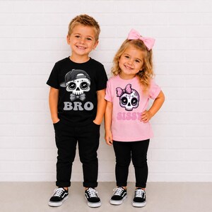May include: A black t-shirt with a graphic of a skull wearing a baseball cap and the text BRO, paired with black pants, and a light pink t-shirt with a graphic of a skull wearing a pink bow and the text SISSY, paired with black pants.