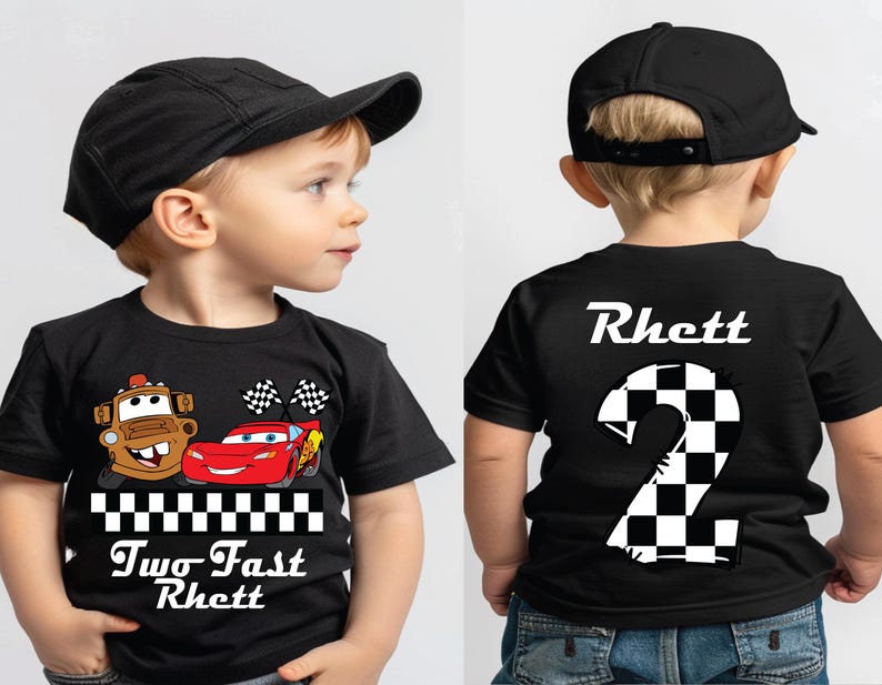 May include: Black t-shirt featuring cartoon characters Mater and Lightning McQueen with checkered flags. The shirt has the text "Two Fast Rhett" on the front and the name "Rhett" and a checkered number 2 on the back. The child is wearing a black baseball cap.
