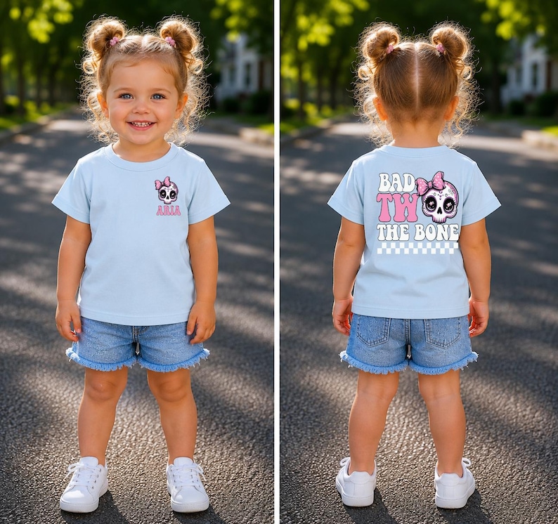 May include: A light blue t-shirt featuring a small skull graphic with a pink bow and the name Aria on the front, and a large skull graphic with a pink bow, the text BAD TO THE BONE, and a checkered pattern on the back, paired with denim shorts.