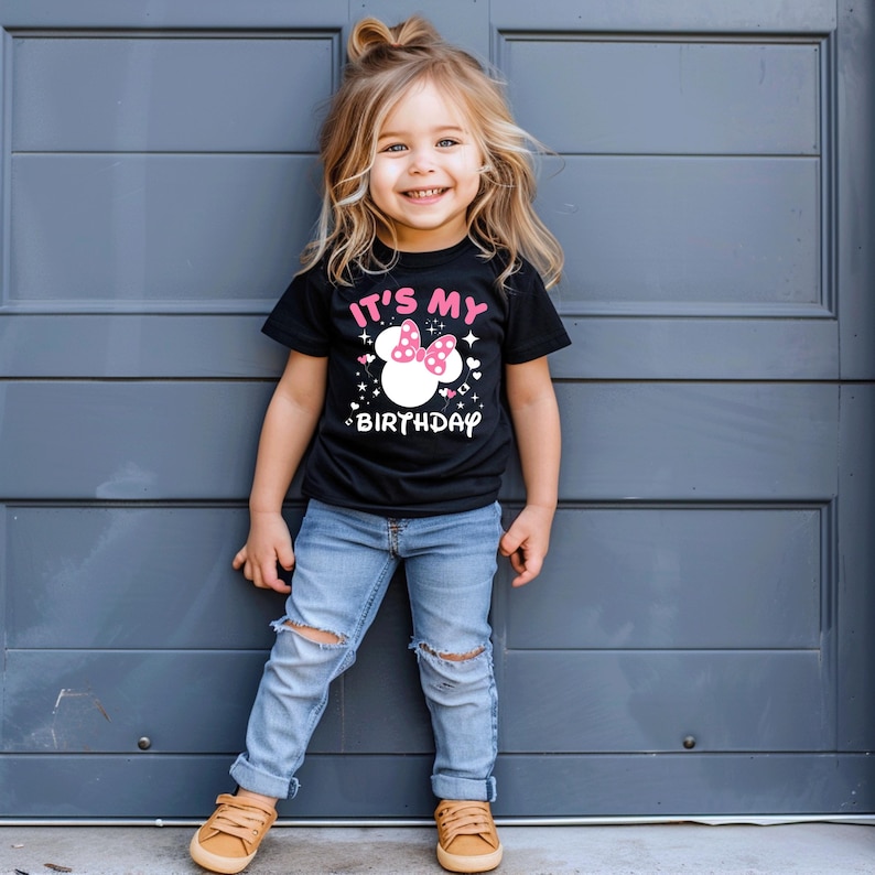 May include: A black t-shirt with the text "IT'S MY BIRTHDAY" and a white Minnie Mouse head graphic with a pink bow. The shirt is worn by a young child with blonde hair and blue jeans.