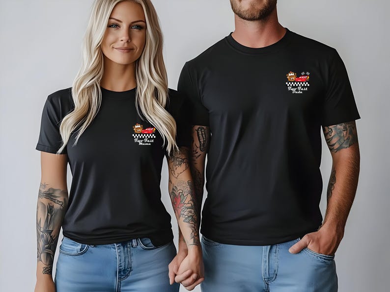 Puede incluir: Camisetas negras con un peque&ntilde;o gr&aacute;fico en el pecho. El gr&aacute;fico presenta un coche de carreras rojo, una bandera a cuadros y el texto "Fast Mama" y "Fast Dada". Las camisetas son usadas por una pareja, ambos con vaqueros azules.