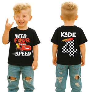 Op de afbeelding: Een zwart T-shirt met korte mouwen, voorzien van een rode raceauto-afbeelding met de tekst "NEED FOUR SPEED" op de voorzijde en de naam "KADE" boven een groot geblokt cijfer "4" op de achterzijde, gedragen door een kind in een lichtblauwe jeans.