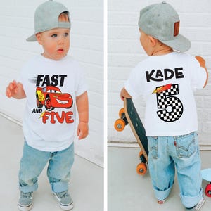 K&ouml;nnte beinhalten: Ein wei&szlig;es kurz&auml;rmeliges T-Shirt mit einer roten Rennwagen-Grafik und dem Text FAST AND FIVE auf der Vorderseite sowie dem Namen KADE mit der Zahl 5 im schwarz-wei&szlig;en Karomuster auf der R&uuml;ckseite, kombiniert mit einer hellblauen Jeans und einer grauen Kappe.