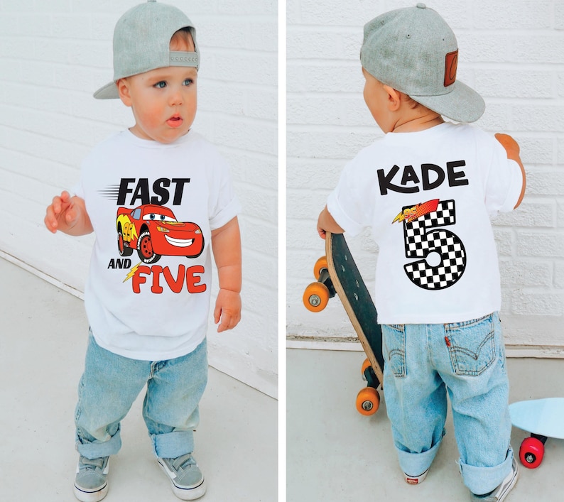 K&ouml;nnte beinhalten: Ein wei&szlig;es kurz&auml;rmeliges T-Shirt mit einer roten Rennwagen-Grafik und dem Text FAST AND FIVE auf der Vorderseite sowie dem Namen KADE mit der Zahl 5 im schwarz-wei&szlig;en Karomuster auf der R&uuml;ckseite, kombiniert mit einer hellblauen Jeans und einer grauen Kappe.