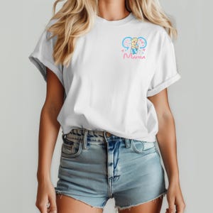 May include: A white short-sleeve t-shirt featuring a small graphic on the left chest. The design includes a cartoon character with blonde hair in a blue dress, framed by light blue mouse ears and pink hearts, with the word Mama written below.