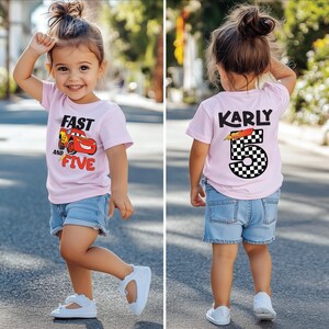 K&ouml;nnte beinhalten: Ein hellrosa T-Shirt mit kurzen &Auml;rmeln, das vorne eine rote Rennwagengrafik mit dem Text Fast and Five zeigt und auf der R&uuml;ckseite den Namen Karly &uuml;ber einer gro&szlig;en Zahl 5 mit schwarz-wei&szlig;em Karomuster, kombiniert mit einer blauen Jeansshorts.