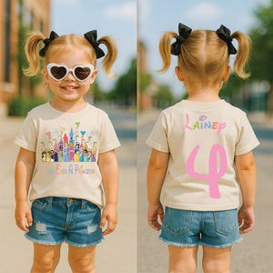 May include: A beige t-shirt with a colorful castle graphic and the text "Forever A Princess." The back of the shirt has the name "Lainey" and the number "4" in pink. The child is wearing denim shorts and heart-shaped sunglasses.
