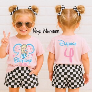 May include: A light pink t-shirt featuring a graphic of a blonde character in a blue dress with the text Birthday Girl and mouse ears. The back displays the name Daphne and the number 4. The outfit includes black and white checkered shorts.