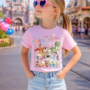 May include: A young person wearing a pink t-shirt with a graphic of Toy Story characters and the text "YOU'VE GOT A FRIEND IN ME". They are also wearing heart-shaped sunglasses and denim shorts.