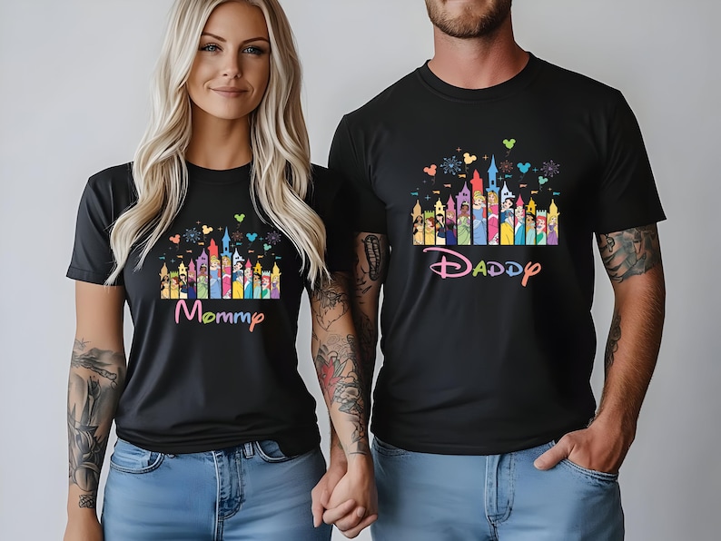 May include: Black t-shirts with a colorful castle design and the words "Mommy" and "Daddy" in a playful font. The design includes various cartoon characters and castle turrets. The shirts are worn by two people.