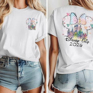 Pu&ograve; includere: T-shirt bianca con un colorato castello Disney e un design a fiocco. La parte anteriore presenta "Mama" e il retro dice "Disney Trip 2026". Il design include colori pastello e uno stile stravagante, perfetto per una vacanza a Disney.