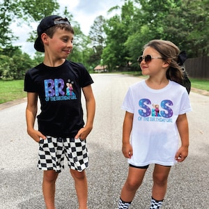 K&ouml;nnte beinhalten: Zwei Kinder tragen passende Geburtstags-T-Shirts. Ein Kind tr&auml;gt ein schwarzes Shirt mit dem Text "BR of the Birthday Girl" und karierten Shorts. Das andere Kind tr&auml;gt ein wei&szlig;es Shirt mit dem Text "S&S of the Birthday Girl".