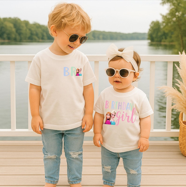 K&ouml;nnte beinhalten: Zwei Kinder in wei&szlig;en T-Shirts und blauen Jeans. Die Shirts zeigen die Aufschrift "BR" und "Birthday Girl" mit einem Cartoon-Bild. Beide Kinder tragen Sonnenbrillen. Im Hintergrund sind ein See und ein wei&szlig;es Gel&auml;nder zu sehen.