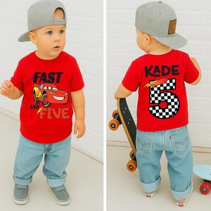 K&ouml;nnte beinhalten: Ein rotes T-Shirt mit einer Grafik eines roten Rennwagens und dem Text FAST AND FIVE auf der Vorderseite sowie dem Namen KADE mit der Zahl 5 im Schachbrettmuster auf der R&uuml;ckseite. Das Outfit umfasst eine hellblaue Jeans und eine graue Baseballkappe.