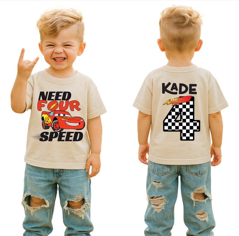 Op de afbeelding: Een beige t-shirt met korte mouwen en een afbeelding van een rode raceauto met de tekst "NEED FOUR SPEED" op de voorkant. De achterkant toont de naam "KADE" boven een groot cijfer "4" met een zwart-wit geblokt patroon en een bliksemschicht.