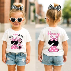 May include: A white t-shirt with a Minnie Mouse design, featuring a large number 2 with pink polka dots and a black outline. The shirt also has the text "Oh, Twoodles". The back of the shirt has the name "Henley" and a similar design.