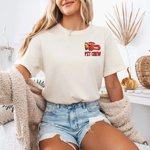 Op de afbeelding: Een cr&egrave;mekleurig t-shirt met korte mouwen en een kleine afbeelding op de linkerborst. De afbeelding toont een rode raceauto met de tekst PIT CREW in dikke rode letters direct onder de illustratie van de auto gedrukt.