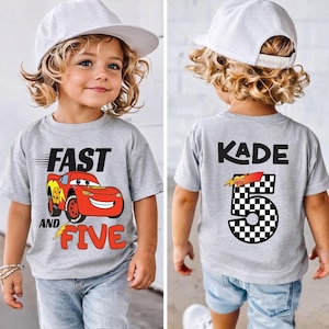 K&ouml;nnte beinhalten: Ein graues T-Shirt mit einem roten Rennwagen-Motiv auf der Vorderseite und dem Text FAST AND FIVE. Auf der R&uuml;ckseite des T-Shirts steht der Name KADE &uuml;ber einer gro&szlig;en Zahl 5 mit Schachbrettmuster und einer kleinen Rennwagen-Grafik.