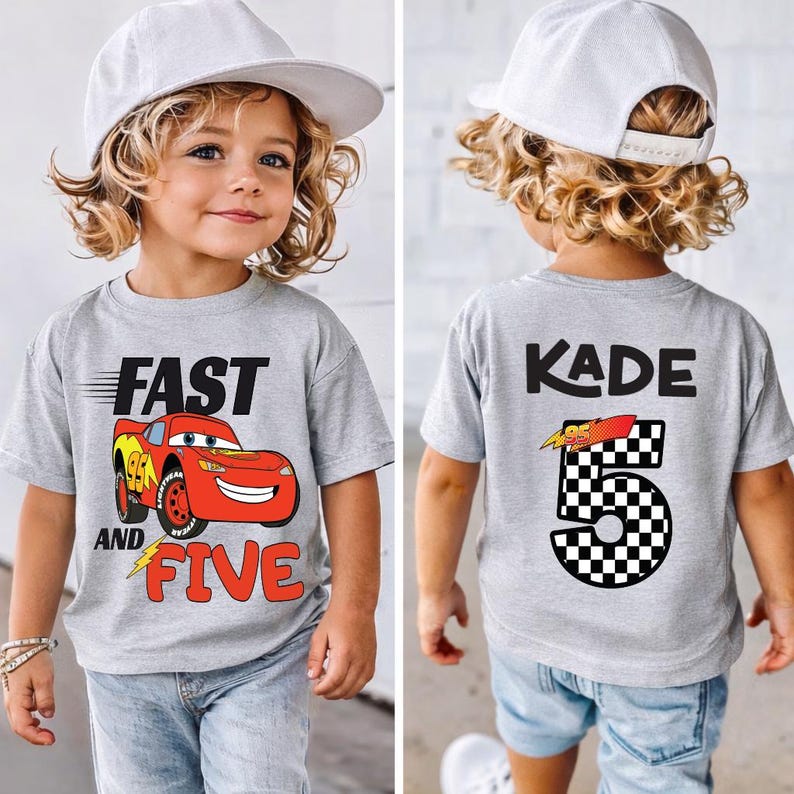 K&ouml;nnte beinhalten: Ein graues T-Shirt mit einem roten Rennwagen-Motiv auf der Vorderseite und dem Text FAST AND FIVE. Auf der R&uuml;ckseite des T-Shirts steht der Name KADE &uuml;ber einer gro&szlig;en Zahl 5 mit Schachbrettmuster und einer kleinen Rennwagen-Grafik.