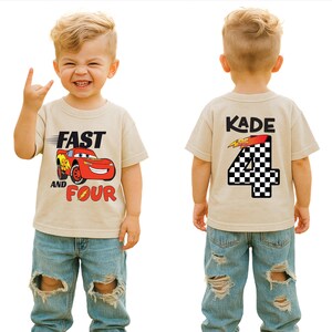 Pu&ograve; includere: Una t-shirt beige a maniche corte con una grafica di auto da corsa rossa sul davanti con il testo FAST AND FOUR. Il retro della maglietta mostra il nome KADE sopra un grande numero 4 con un motivo a scacchi bianco e nero e un fulmine.