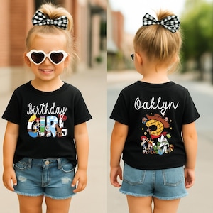 K&ouml;nnte beinhalten: Schwarzes T-Shirt mit dem Text "Birthday Girl" und Zeichentrickfiguren. Die Vorderseite des Shirts hat ein farbenfrohes Design. Auf der R&uuml;ckseite des Shirts steht der Name "Oaklyn" und weitere Zeichentrickfiguren. Das M&auml;dchen tr&auml;gt Jeansshorts und herzf&ouml;rmige Sonnenbrillen.