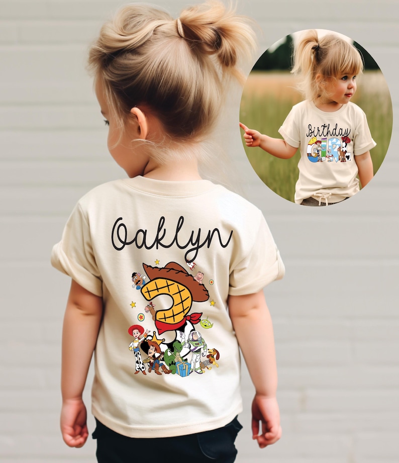 K&ouml;nnte beinhalten: Ein beiges T-Shirt mit dem Namen "Oaklyn" in schwarzer Schrift auf der R&uuml;ckseite. Das Shirt zeigt eine farbenfrohe Grafik von Toy Story-Charakteren, darunter Woody und Buzz Lightyear, mit einer gro&szlig;en "2".