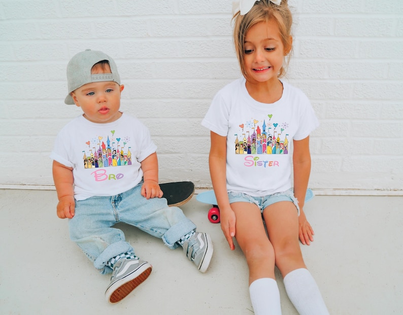 May include: Two children wearing white t-shirts with a colorful castle design and the words "Bro" and "Sister". The boy wears a gray cap, blue jeans, and gray sneakers. The girl wears denim shorts and white socks.