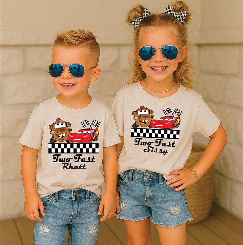 Puede incluir: Dos ni&ntilde;os con camisetas beige con un dise&ntilde;o de coche de dibujos animados. El dise&ntilde;o incluye un coche marr&oacute;n, un coche rojo y banderas a cuadros. El texto "Two Fast" y un nombre est&aacute;n impresos debajo. Ambos ni&ntilde;os llevan gafas de sol.