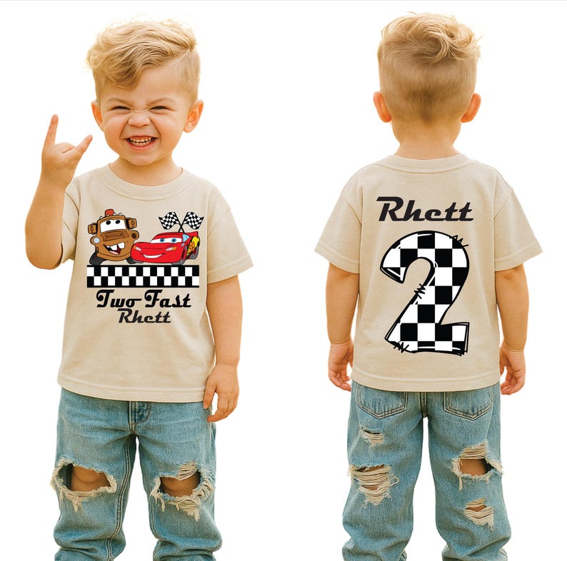 May include: A tan t-shirt featuring a cartoon car design with the text "Two Fast Rhett" on the front and a checkered number 2 on the back. The shirt is paired with blue denim jeans.