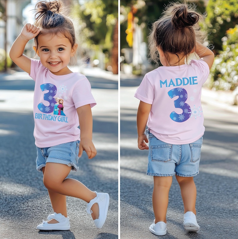 K&ouml;nnte beinhalten: Ein junges M&auml;dchen tr&auml;gt ein hellrosa T-Shirt mit der Zahl 3 in Blau und wei&szlig;en Schneeflocken und den Worten &bdquo;BIRTHDAY GIRL&ldquo;. Sie tr&auml;gt auch Jeansshorts und wei&szlig;e Schuhe. Auf der R&uuml;ckseite des Shirts stehen der Name &bdquo;MADDIE&ldquo; und die Zahl 3.