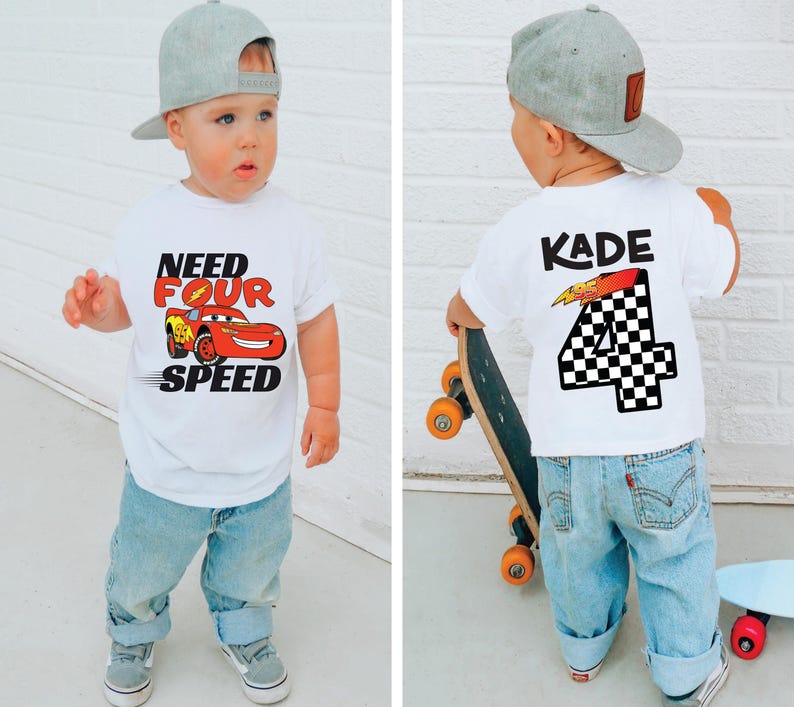 Op de afbeelding: Een wit T-shirt met korte mouwen voorzien van een rode raceauto-afbeelding met de tekst "NEED FOUR SPEED" op de voorzijde en de naam "KADE" boven een groot geblokt cijfer "4" op de achterzijde, gecombineerd met een lichtblauwe jeans en een grijze pet.