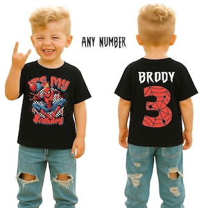 May include: Black t-shirt featuring a Spider-Man graphic and the text "It's My Birthday". The back of the shirt has the name "Brody" and the number "3" with a spiderweb design. The child is wearing blue jeans.