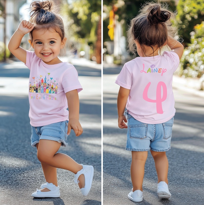 May include: A young child wearing a light pink t-shirt and denim shorts. The front of the shirt features a colorful graphic of a castle and characters, with text below. The back of the shirt has a name and the number 4.