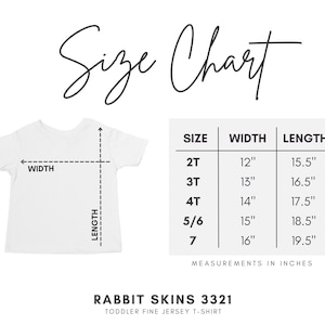 May include: A white toddler t-shirt size chart for Rabbit Skins 3321. The graphic shows a t-shirt outline with width and length arrows and a table listing sizes 2T through 7 with corresponding measurements in inches. Text reads Size Chart.