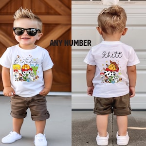 May include: White t-shirt with a colorful graphic featuring cartoon characters and the word "Birthday BOY". The back of the shirt has the name "Rhett" and a similar graphic. The child is wearing brown shorts and white sneakers.