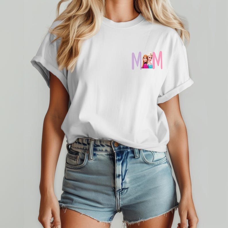 K&ouml;nnte beinhalten: Wei&szlig;es T-Shirt mit umgekrempelten &Auml;rmeln, das das Wort "MOM" in einem lila-rosa Farbverlauf und ein Cartoon-Bild von zwei M&auml;dchen zeigt. Das T-Shirt besteht aus einem weichen Material und eignet sich f&uuml;r Freizeitkleidung.