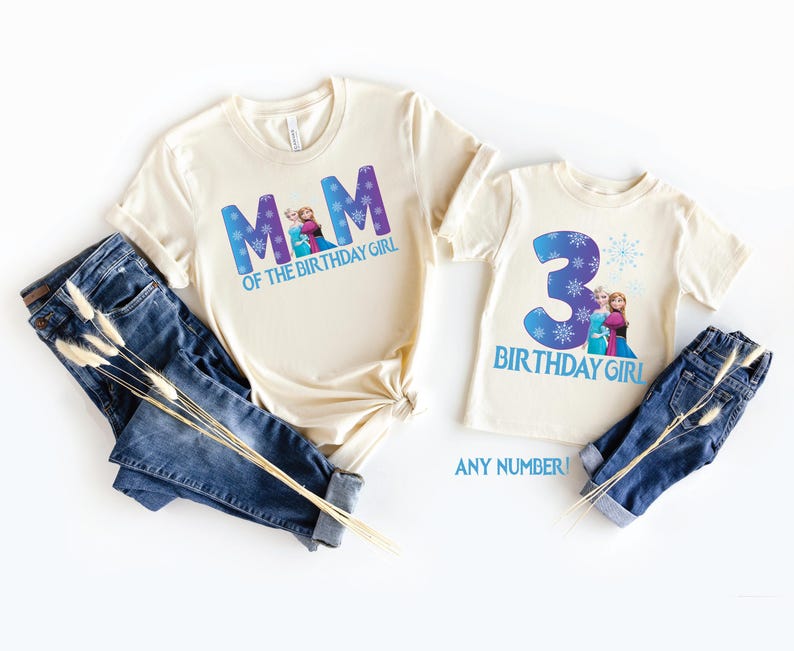 K&ouml;nnte beinhalten: Zwei cremefarbene T-Shirts mit blauem Text und Grafiken. Auf einem Shirt steht "MOM OF THE BIRTHDAY GIRL" und auf dem anderen "3 BIRTHDAY GIRL". Beide Shirts sind mit blauen Jeans kombiniert. Der Text "ANY NUMBER!" ist ebenfalls sichtbar.