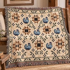 May include: A woven throw blanket featuring a repeating pattern of blue chickens, brown eight-pointed stars, and small green floral motifs on a cream-colored background. The blanket has a decorative border and fringed edges on the top and bottom.