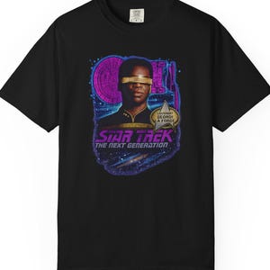 May include: Black t-shirt featuring a graphic of a Star Trek character with the text "STAR TREK THE NEXT GENERATION." The design includes a portrait of the character with a gold visor and a purple and blue background.