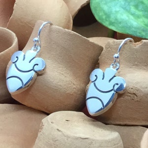 May include: A pair of silver dangle earrings featuring a heart-shaped design. The heart has a stylised pattern with swirls and lines.