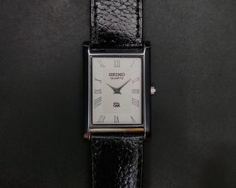 Vintage, generalüberholte Seiko Slim Quartz Herrenuhr mit weißem Zifferblatt, schwarzem Armband und 26 mm Durchmesser (rechteckig).