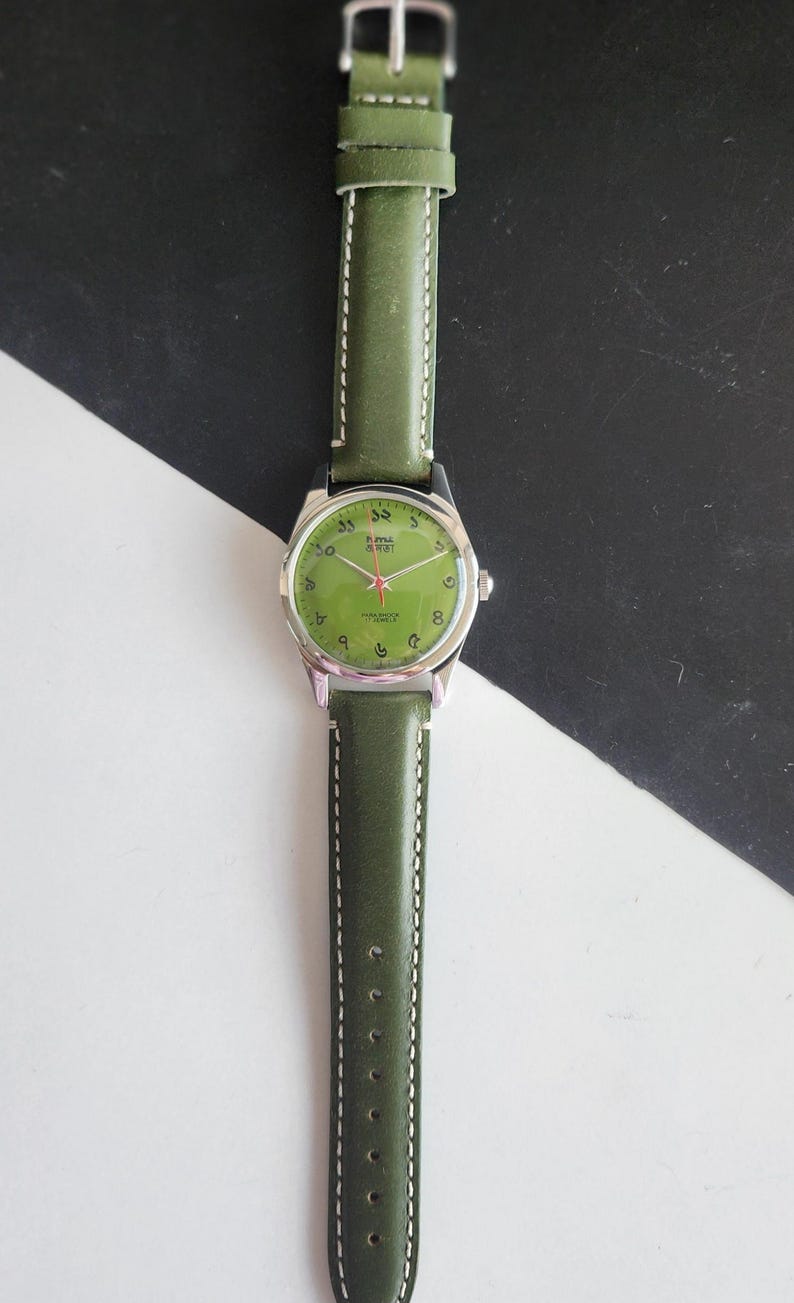 May include: A wristwatch with a green leather band and a silver-colored case. The watch face is green with black numerals and hands. The band is stitched with white thread.