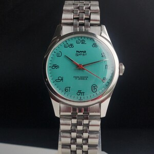 May include: A silver-toned wristwatch with a teal face and a matching silver band. The watch face features black text and numerals, with red second hand. The watch is labeled "PARA SHOCK 17 JEWELS".
