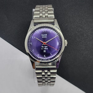Könnte beinhalten: Eine silberfarbene Armbanduhr mit einem lila Zifferblatt und einem silbernen Armband. Das Zifferblatt der Uhr hat Text in einer Fremdsprache und rote Zeiger. Die Uhr hat ein rundes Zifferblatt und eine silberne Krone. Das Armband besteht aus kleinen, verbundenen Metallgliedern.