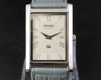 Relógio masculino Seiko Slim vintage restaurado, com mostrador branco e pulseira cinza, 26 mm, quartzo, retangular.